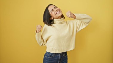 Neşeli İspanyol bir kadın, izole edilmiş sarı bir arka planda güven içinde poz veriyor, rahat bir moda ve enerjik bir enerji sergiliyor..