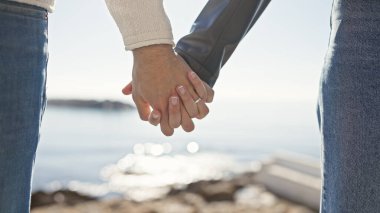 Couple holding hands at the seaside signifies love and connection amidst a beautiful ocean backdrop. clipart