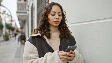 Şehir caddesinde arka planda binalar olan akıllı telefon kullanan bir kadın.