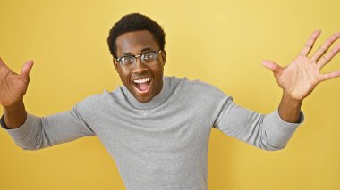 Gözlüklü heyecanlı Afrikalı Amerikalı adam sarı arka planda kutlama yapıyor, kolları açık..