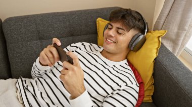 Evdeki kanepede uzanmış video oyunu oynayan İspanyol genç adam.