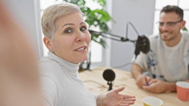 A woman talking into a microphone on a radio show with a smiling man in a studio setting clipart