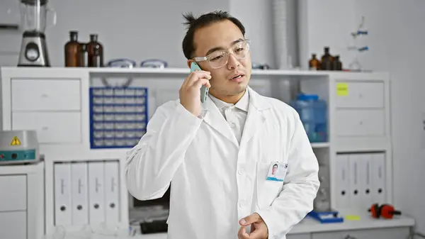 Young chinese man scientist talking on smartphone at laboratory