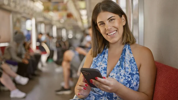 陽気で美しいヒスパニック女性は 空の地下鉄に一人で座って 幸せに彼女のスマートフォンを使用して 都市の交通機関で肯定的な時間を過ごしています — ストック写真