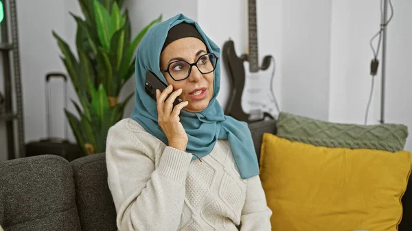 一个戴头巾的成熟女人坐在现代客厅的沙发上 一边打电话一边聊天 — 图库照片