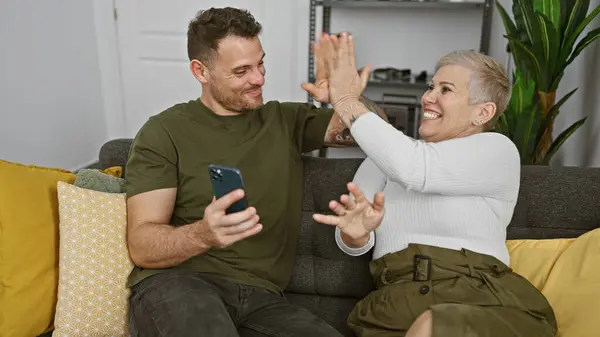 Adult man and woman sharing a joyful moment with a high-five in a cozy living room setting, evoking happiness and togetherness.