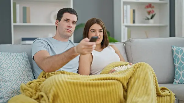 Beautiful couple watching movie covering with blanket at home