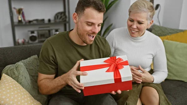 一个男人和一个女人在沙发上共度快乐时光 兴奋地在舒适的客厅里打开一个红色礼品盒 — 图库照片