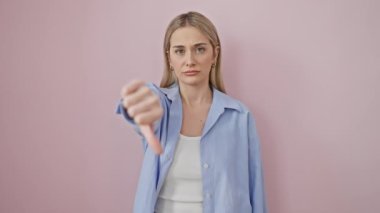 Gömlekli kızgın genç sarışın negatif baş parmak hareketi gösteriyor, kötü ifade de mutsuz iğrenme gösteriyor. Pembe arkaplan üzerinde izole