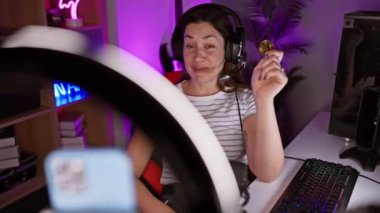 Mavi gözlü ve parlak gülüşlü neşeli genç kadın rahat bir oyun odasında Bitcoin başarı videosu kaydediyor.