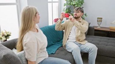 Erkek, evin içinde gülümseyen kadını fotoğraflıyor, sıcak bir oturma odasında sevgi dolu bir anı yakalıyor..