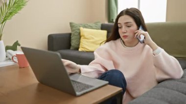 Genç bir kadın, rahat oturma odasında dizüstü bilgisayarı ve telefonu olan, modern bir telekomünikasyon sergiliyor..