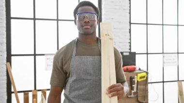 Başarılı tezahürat, Afro-Amerikan genç adam, neşeli bir marangoz, kereste tutuyor ve marangozluk başarısını kazanan bir gülümseme ve kapalı stüdyosunda mutlu bir ifadeyle kutluyor.