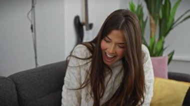 Süveter giyen genç bir İspanyol kadın, bisikletçisi Yorkshire Teriyeriyle kanepede kaynaşmaktan hoşlanıyor..