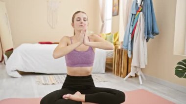 Huzurlu bir yatak odası ortamında yoga yapan huzurlu genç bir kadın, sağlığını ve iç huzurunu gösteriyor..