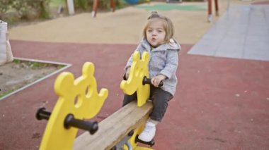Sarı bir tahterevallide oynayan sevimli sarışın kız güneşli bir parkta masumiyetini ve açık havada çocukluğunu gösteriyor..