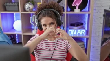 Kıvırcık saçlı, gülümseyen İspanyol kadın elleri ile kalp sembolü oluşturuyor, oyun odasında romantik bir konsept için aşkı gösteriyor.