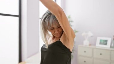 Gri saçlı olgun bir kadın modern yatak odasında koltuk altını inceliyor..