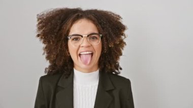 Neşeli, kıvırcık saçlı ve komik bir ifadesi olan genç İspanyol kadın, dilini izole edilmiş beyaz bir arka plana yapıştırıyor, mutluluk ve pozitiflik saçıyor.