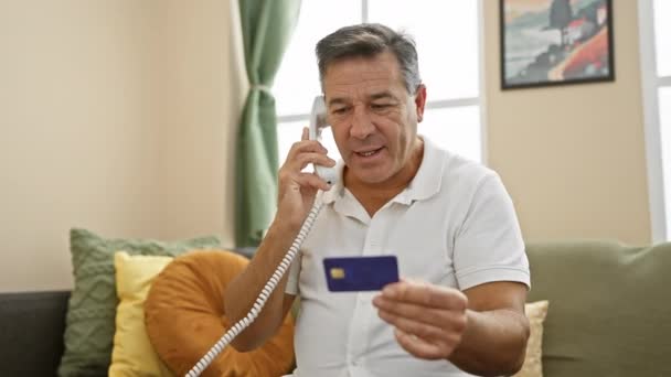 Mężczyzna Średnim Wieku Trzyma Kartę Kredytową Podczas Rozmowy Telefonicznej Salonie — Wideo stockowe