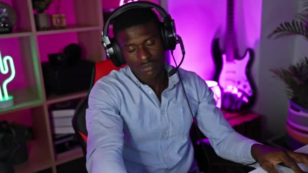 一个戴着耳机 专心致志的非洲男人晚上在一个充满活力的游戏室的电脑前工作 — 图库视频影像