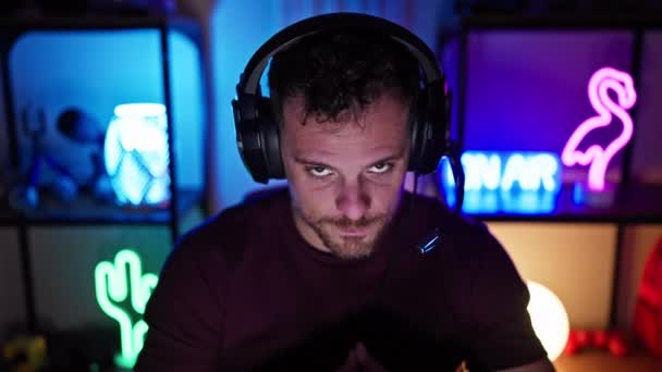一个留着胡子的男人 晚上头戴耳机在霓虹灯下的游戏室里 散发出一种专注的 熟悉技术的氛围 — 图库视频影像
