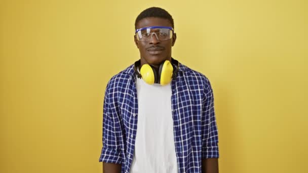 アフリカ系アメリカ人男性は 健康的な歯医者の笑顔で 安全眼鏡に立って ポジティブで幸せでフレンドリーに見えます 陽気な黄色の背景に隔離された — ストック動画