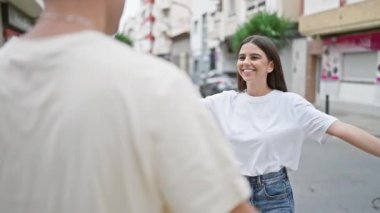 Gülümseyen bir kadın, sakin bir şehir sokağında bir erkeği kucaklıyor, şehir ortamında aşkı ve arkadaşlığı canlandırıyor.