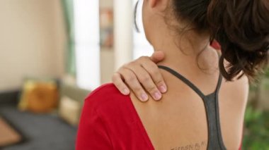 Kırmızı bluzlu İspanyol kadın sırtına dokunuyor, evde acı ya da rahatsızlık gösteriyor..