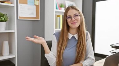 Ofis sunumunda gülümseyen ve gülümseyen genç sarışın iş kadını neşeli bir el hareketiyle ürünü güvenle sergiliyor..