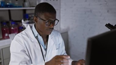 Laboratuvar önlüğü giyen odaklanmış Afrikalı adam laboratuvar ortamında bilgisayardaki verileri analiz ediyor.