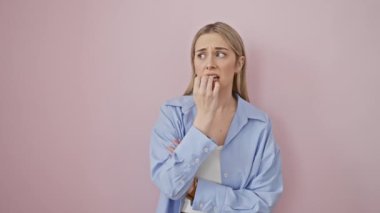 Gergin genç sarışın kadın endişeli görünüyor, pembe izole edilmiş arka planda tırnak yiyor.