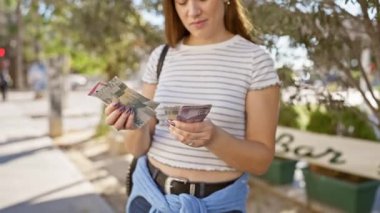 Genç bir kadın yeşil yapraklı güneşli bir parkta Endonezya rupiasını inceliyor..