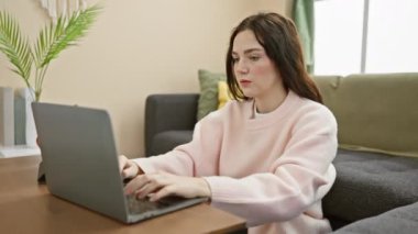 Genç bir kadın evinde, rahat bir oturma odasında dizüstü bilgisayar ve akıllı telefon kullanıyor..