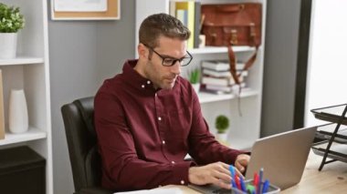 Yakışıklı sakallı adam gözlük çıkarıyor ve modern ofis ortamında esniyor, iş yerinde rahatlık gösteriyor..