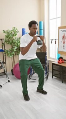 Fizik tedavi kliniğinin spor salonunda dambılla egzersiz yapan odaklanmış bir Afrikalı Amerikalı..