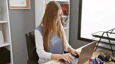 Güzel sarışın iş adamı, mutluluğun tadını çıkarıyor, kollarını başının arkasına uzatmış, ellerini boynuna uzatmış, ofis odasında rahatlatıcı bir anın tadını çıkarıyor, neşeli bir gülümseme sergiliyor.