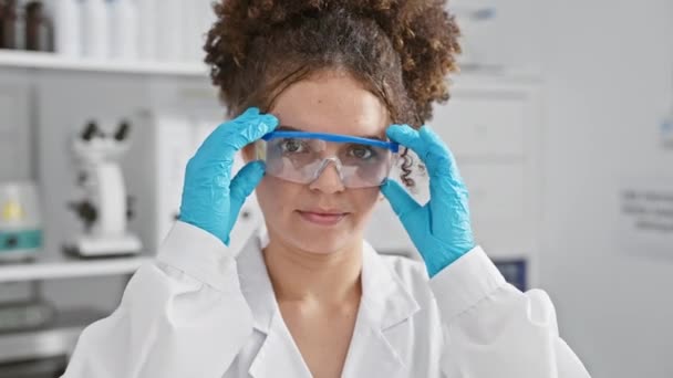 실험실에서 매력적인 히스패닉 여성은 전문성과 전문성을 묘사하는 미소로 장비를 검사합니다 — 비디오