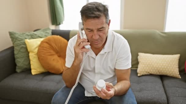 一个成熟的男人在舒适的客厅里检查药瓶时 在电话里交谈 — 图库视频影像