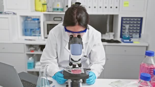 笑顔の女性科学者は 現代の実験室で顕微鏡の下の標本を検査し 医療研究におけるプロフェッショナリズムと専門知識を描写しています — ストック動画