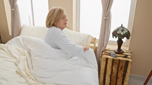 Starsza Kobieta Piżamie Rozciąga Plecy Przebudzeniu Jasnym Wnętrzu Sypialni Domu — Wideo stockowe