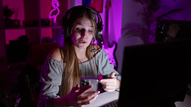 一个心烦意乱的年轻女人 晚上在室内的游戏室里 带着耳机用智能手机 — 图库视频影像