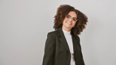 Kıvırcık saçlı neşeli genç İspanyol kadın zafer işareti olarak V 'yi gösteriyor ve parlak bir gülümseme beyaz arka planda izole bir şekilde duruyor, kendinden emin başarıyı somutlaştırıyor..