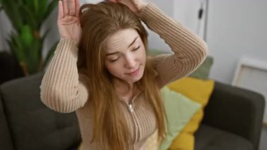 Şüpheci ama oyuncu, genç sarışın kadın evde elleriyle alaycı bir şekilde tavşan kulağı hareketi yapıyor. Paskalya tavşanı konsepti rahat oturma odası ortamında hazırlanır..