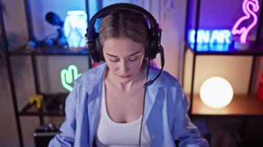 Akşamları renkli bir oyun odasında kulaklık takan, odaklanmış beyaz bir kadın.