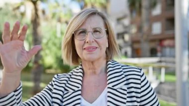 Güneşli bir parkta yeşil gözlükleriyle gülümseyen zarif son sınıf öğrencisi kadın.