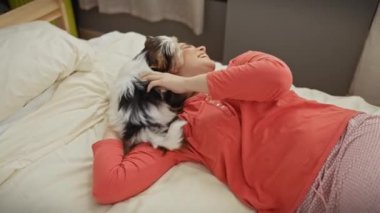 Genç bir kadın, sıcak bir yatak odasında bisikletli Yorkshire Teriyeri 'ni severek okşarken bir yatakta dinleniyor..