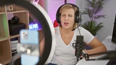 Neşeli orta yaşlı sarışın kadın oyun odasını sallıyor, güvenli bir şekilde işaret veriyor parmakları video çağrısında, sıcak gülümsemeyle pozitif titreşimler yayıyor.
