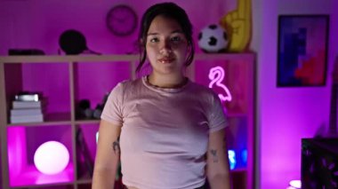 Genç bir İspanyol kadın, geceleri neon ışıklı bir oyun odasında kollarını kavuşturarak güvenle ayakta duruyor..