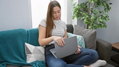 Esmer saçlı neşeli bir kadın oturma odasındaki kanepesinde rahatça oturur ve dizüstü bilgisayarını kapatır..